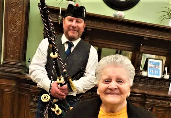 Wheatlands - Lady smiling with Bagpiper behind