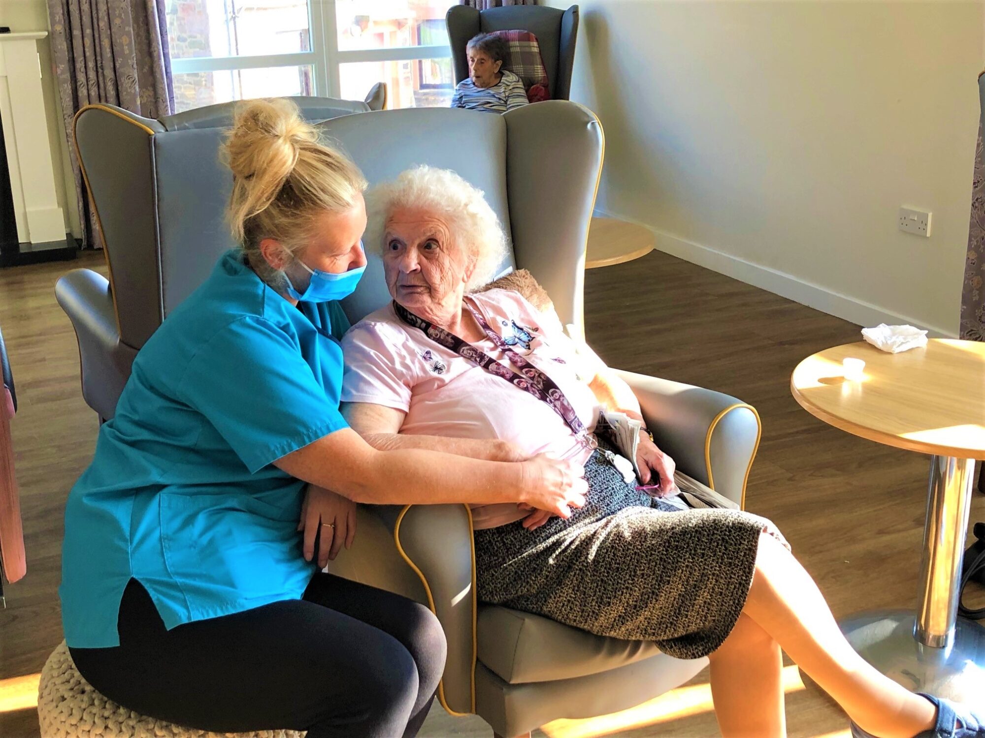 Care assistant sat beside a resident and holding her hand