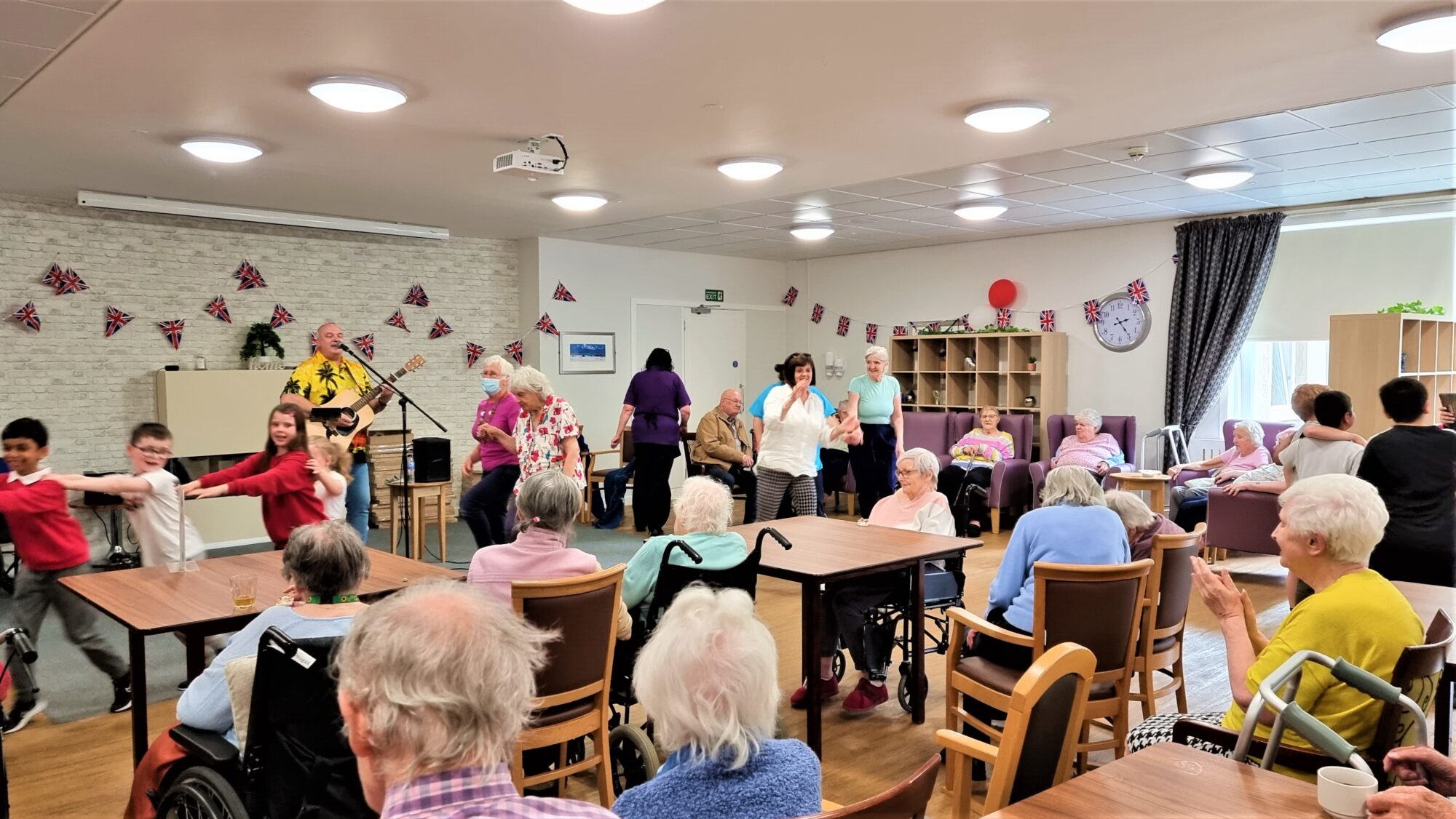 children and residents dancing with singer at care home party