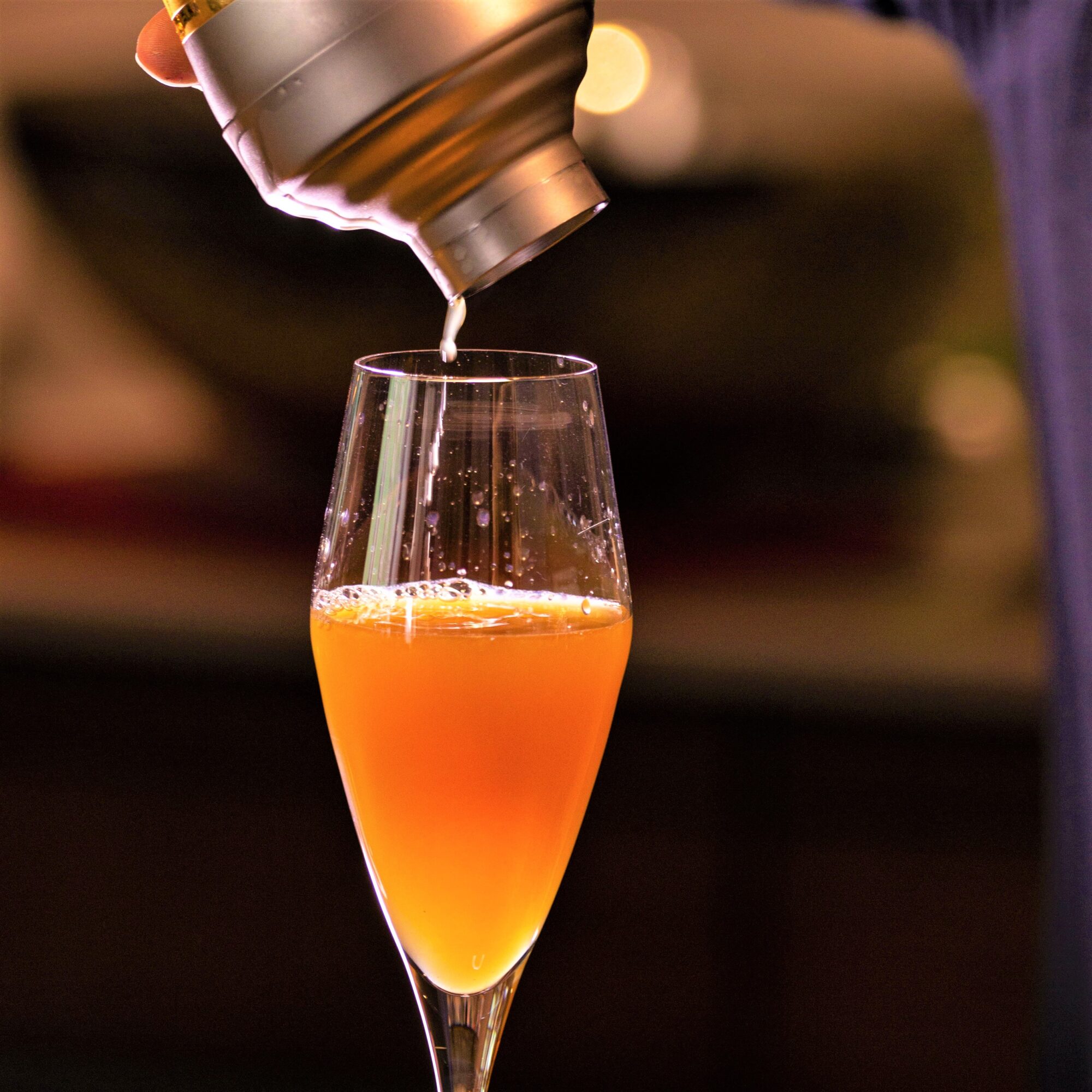 cocktail shaker pouring into glass of peach bellini