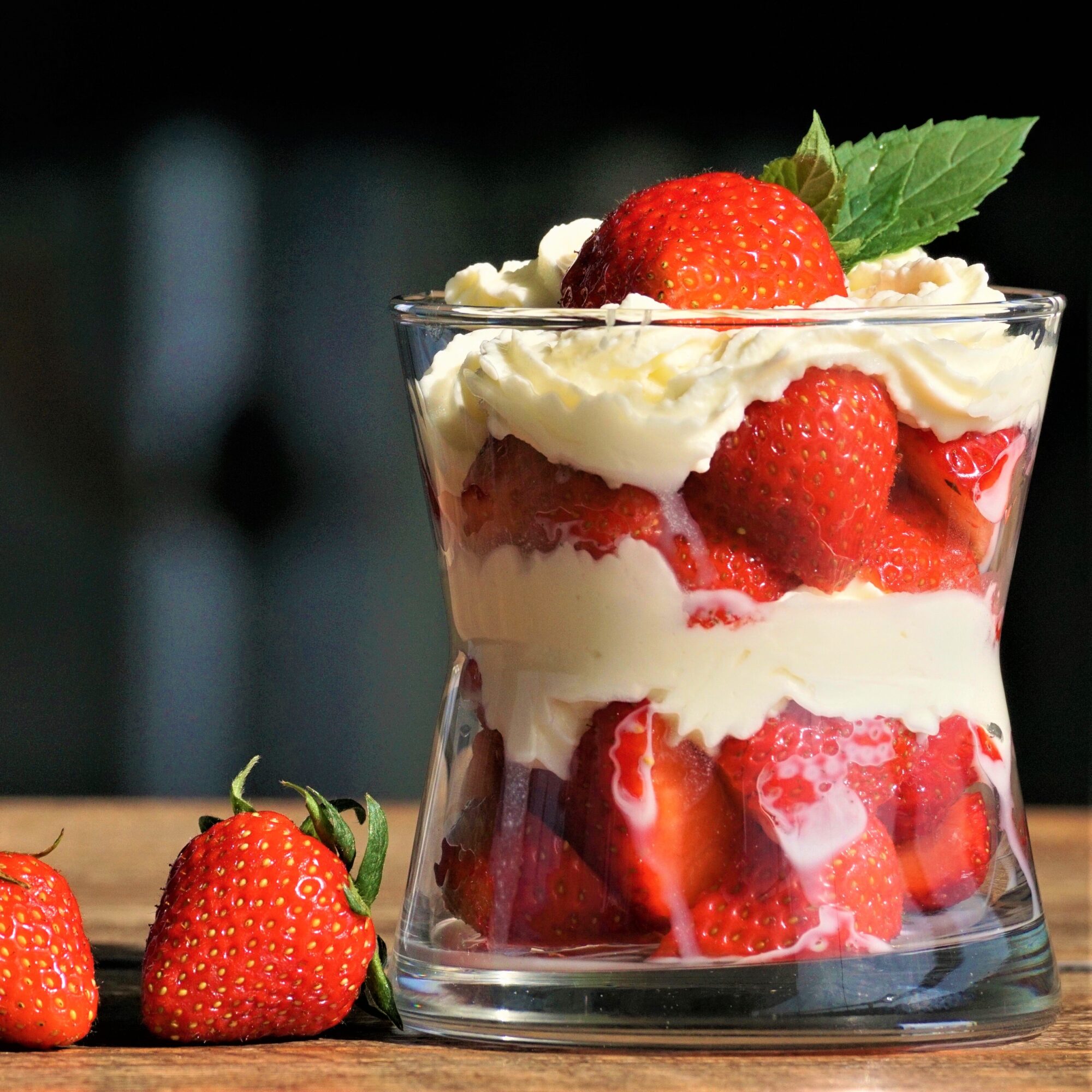 strawberries and cream layered in a class with two strawberreis by the side