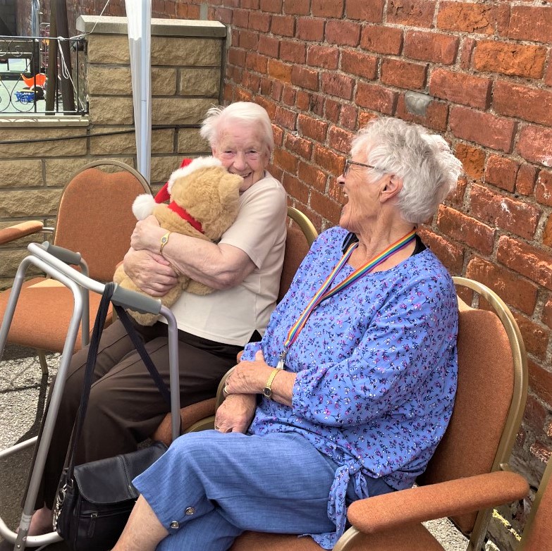 two ladies one hugging a teddy bear at a community event