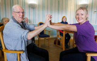 Carer and resident, gentleman and lady sat facing holding hands
