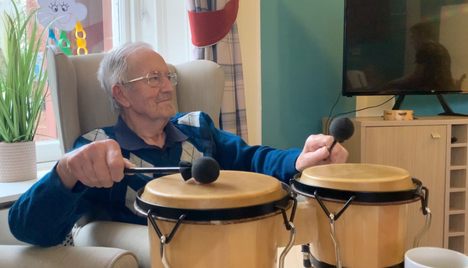 An image of a Balhousie resident playing the bongos at a music therapy session.